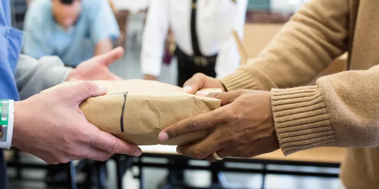 Hands delivering and receiving prison care kit. 