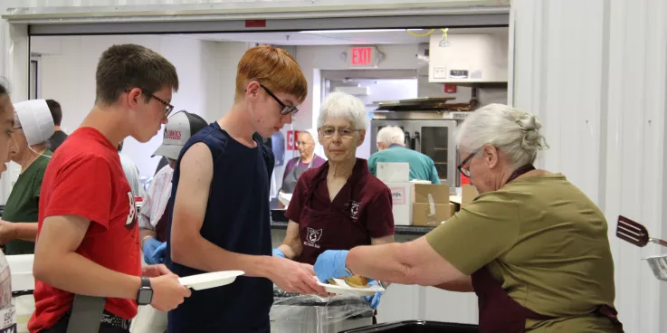 woman serving pancakes to two boys