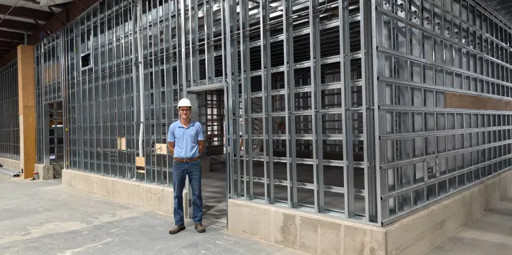 man in hard hat stands in front of a wall of steel studs under construction