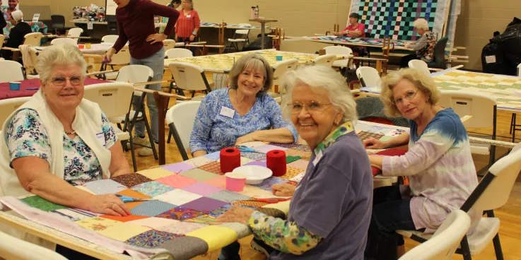 group of women sit around comforter and smile at camera