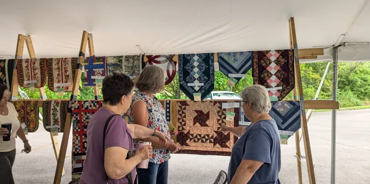 Women admiring quilts on a rack