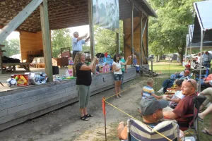 An auctioneer stands on an outdoor stage. Two women are down below displaying toys that are for auction.