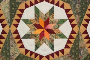 A close up of a quilt featuring a star shape made up of white, green, yellow and red fabric.
