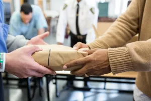 Hands delivering and receiving prison care kit. 