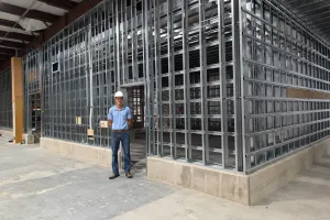 man in hard hat stands in front of a wall of steel studs under construction