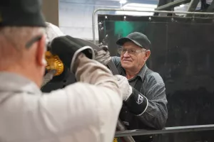 Two men lift a heavy object. The man facing the camera is wearing a black hat and dark clothes.