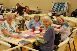 group of women sit around comforter and smile at camera