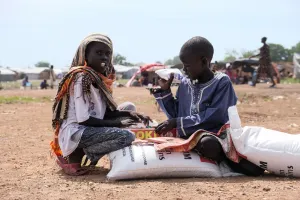 Zero Mawang Juch  (left) and Sudan Koang Ruei at the distribution site with a portion of food supplies. Each bag of sorghum is about 15kgs, so it is heavy for program participants to carry on their he