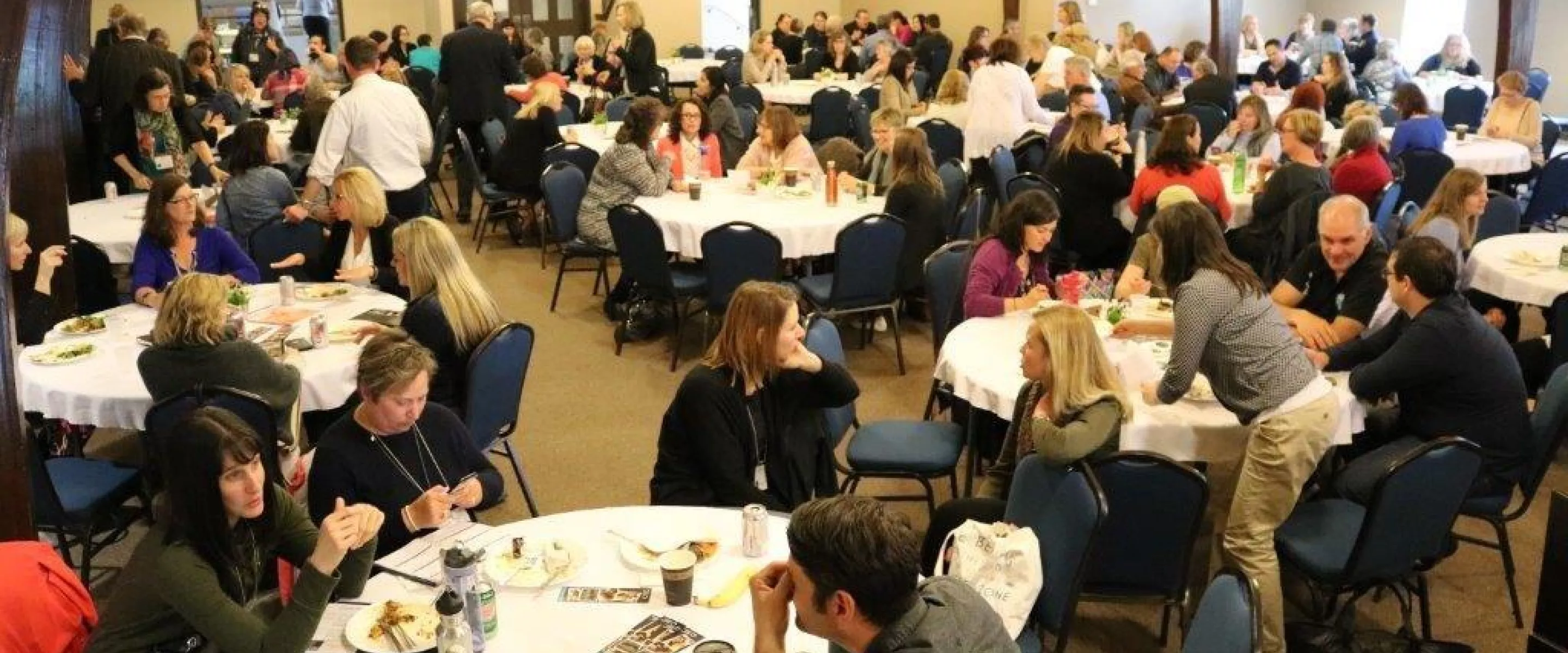 A group of people discussing around several round tables in a large room.