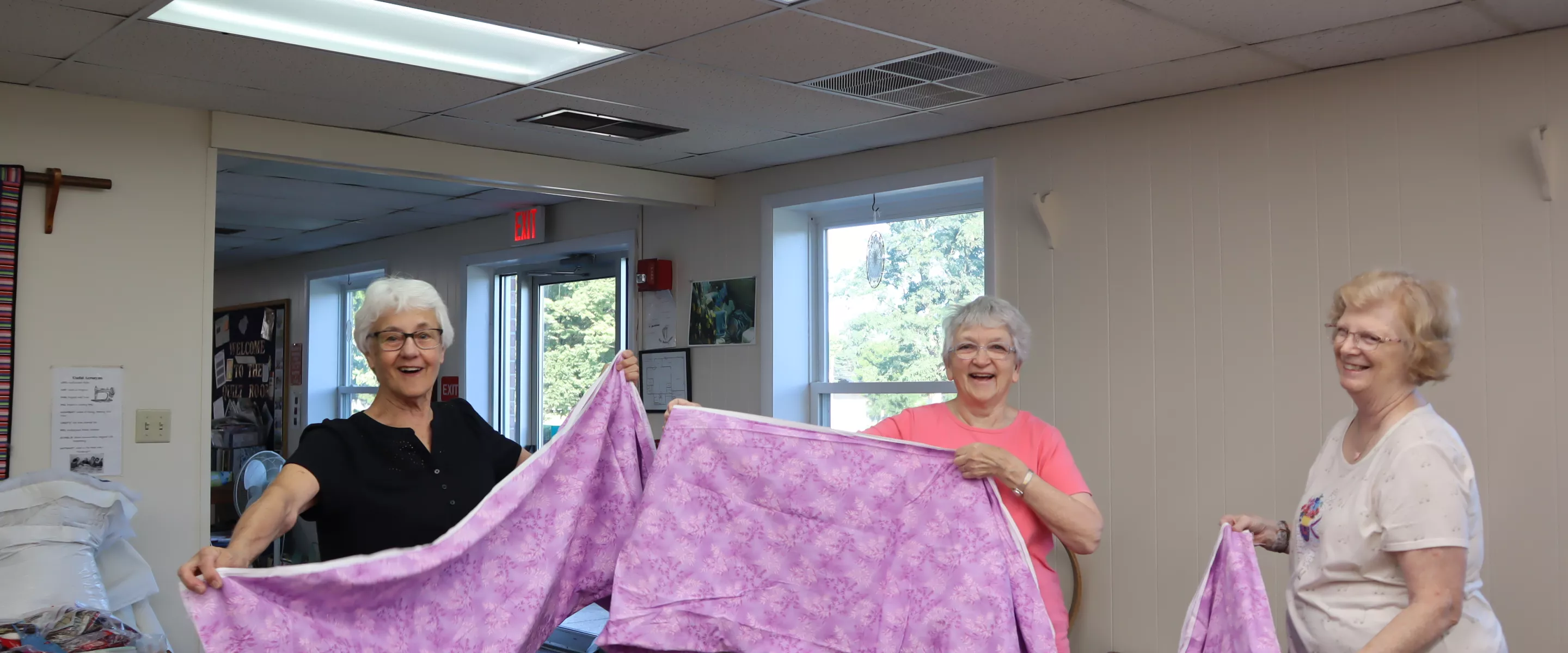 three women hold up a piece of pink fabric