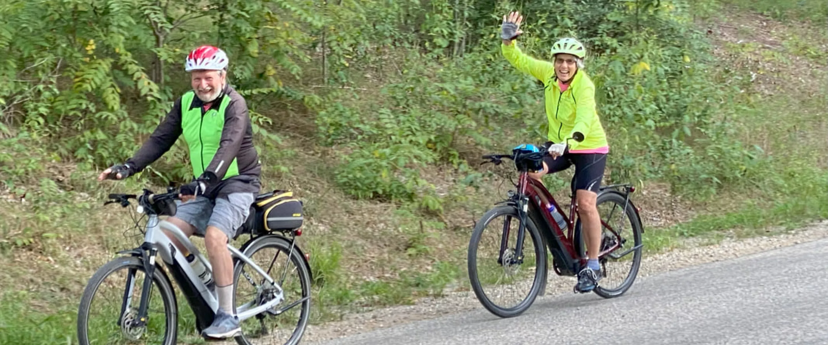 two people riding bicycles wave to the camera