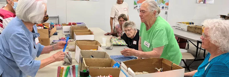 women stand around table putting together school kits