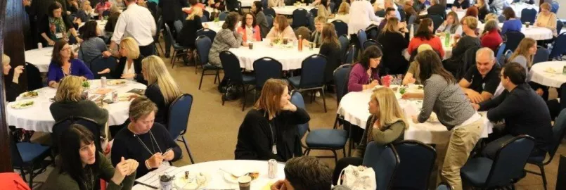 A group of people discussing around several round tables in a large room.