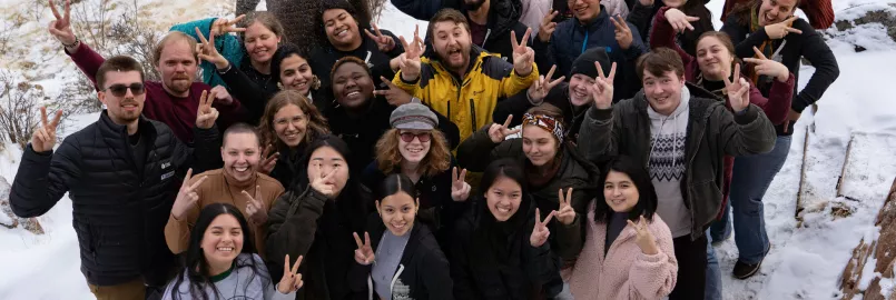 Young adults stand in a group pose in the snow.