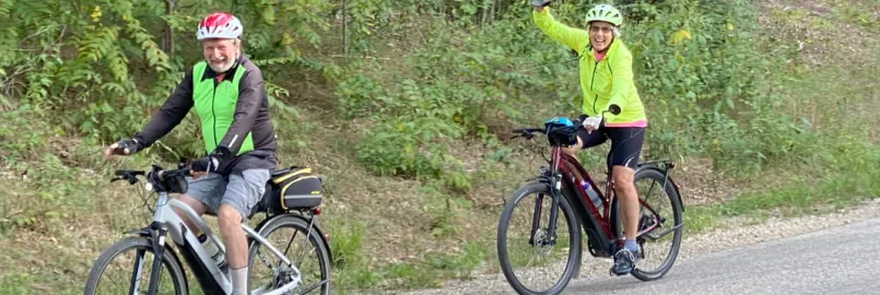 two people riding bicycles wave to the camera