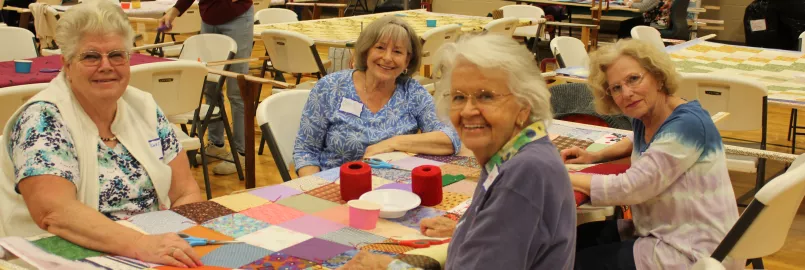 group of women sit around comforter and smile at camera