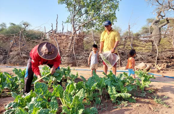 Two people work in a garden in Bolivia. There are two children in the background