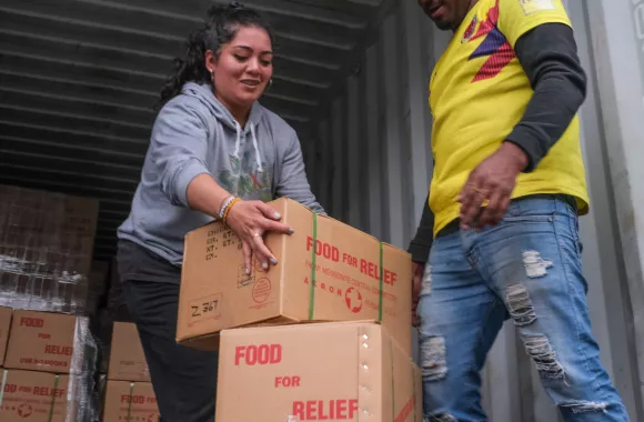 A woman stacks moves boxes out of a shipping container and stacks them on top of each other.