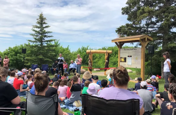 Two people stand in front of a large crowd sitting on lawn chairs