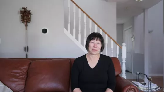 A woman with short, dark hair and a black shirt sits on a leather couch in her living room.