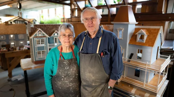 Sharon and Norm Ewert stand in front of wooden dollhouses.