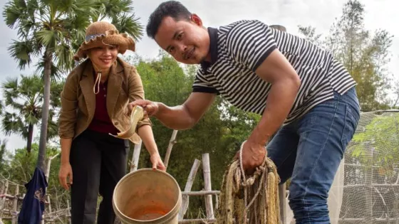 Two people standing for a photo. One holds a bucket and the other holds a fish