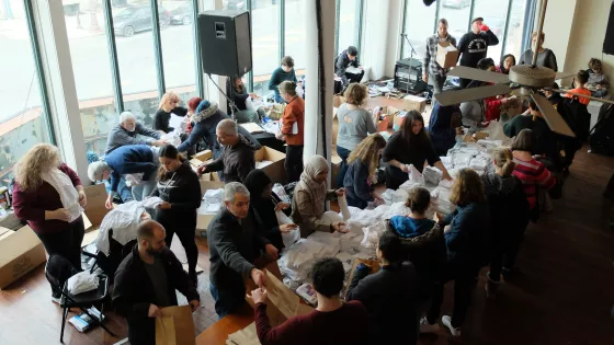 An overview perspective of a large group of people working on a makeshift assembly line on two long tables.