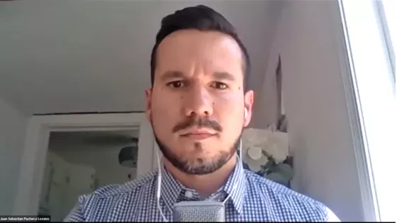 A young man with a beard and headphone speaks into the camera during a webinar on zoom