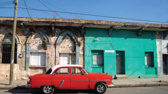 Old red car parked in front of block of residences.