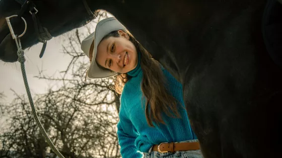 A woman smiling standing with her hand resting on a horse