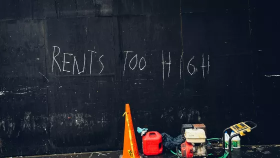 black painted wall with words "rents too high" written with white chaulk