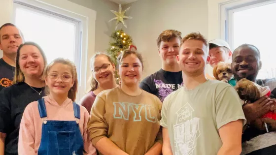 Family of eight stand with an IVEP participant in front of a Christmas tree.