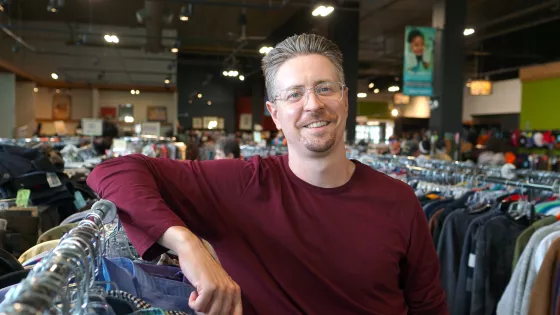 Smiling man leaning on clothing rack