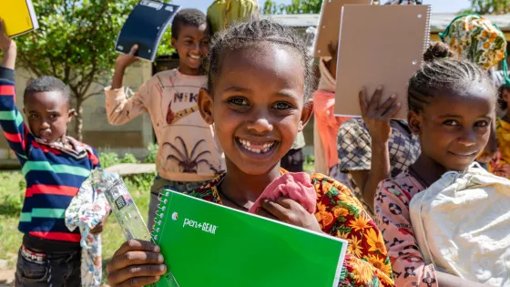 Girl holding notebook while surrounded by other students holding notebooks.