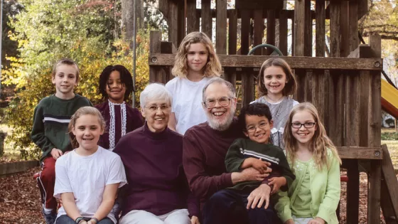 Marilyn and Bill Brown, MCC donors based in Berea, Kentucky, sit on a park bench with their seven grandchildren.