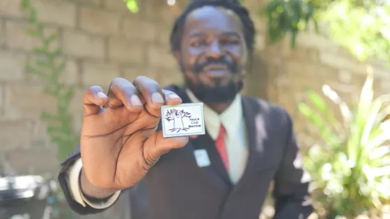 Zebron Mwale holds his badge to signify his Peace Club membership in April 2021. Mwale joined a Peace Club program while serving his sentence in a Zambian prison. He credits Peace Clubs with changing
